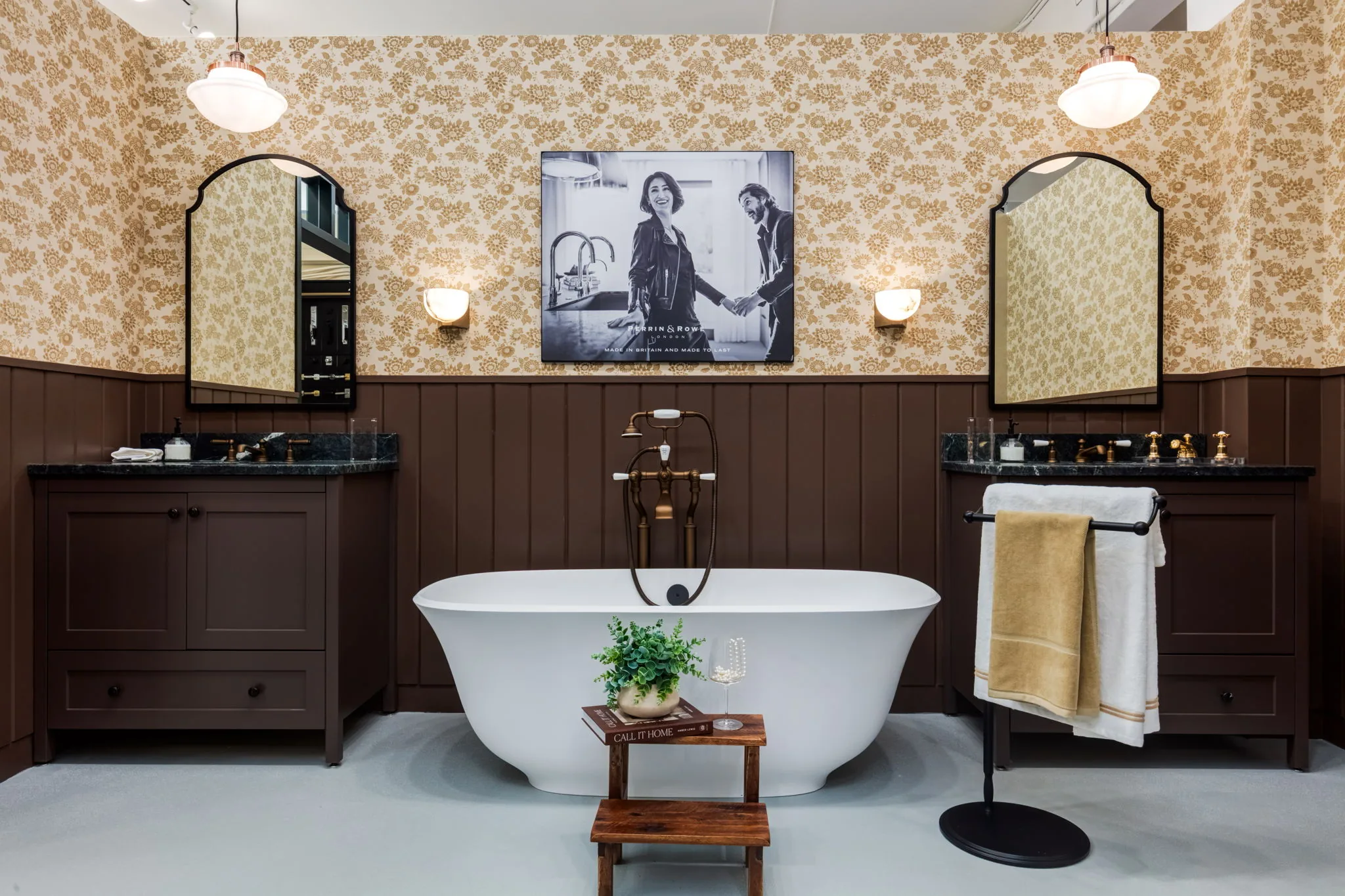 Showroom bathroom display with a freestanding tub, floral wallpaper and brass fixtures