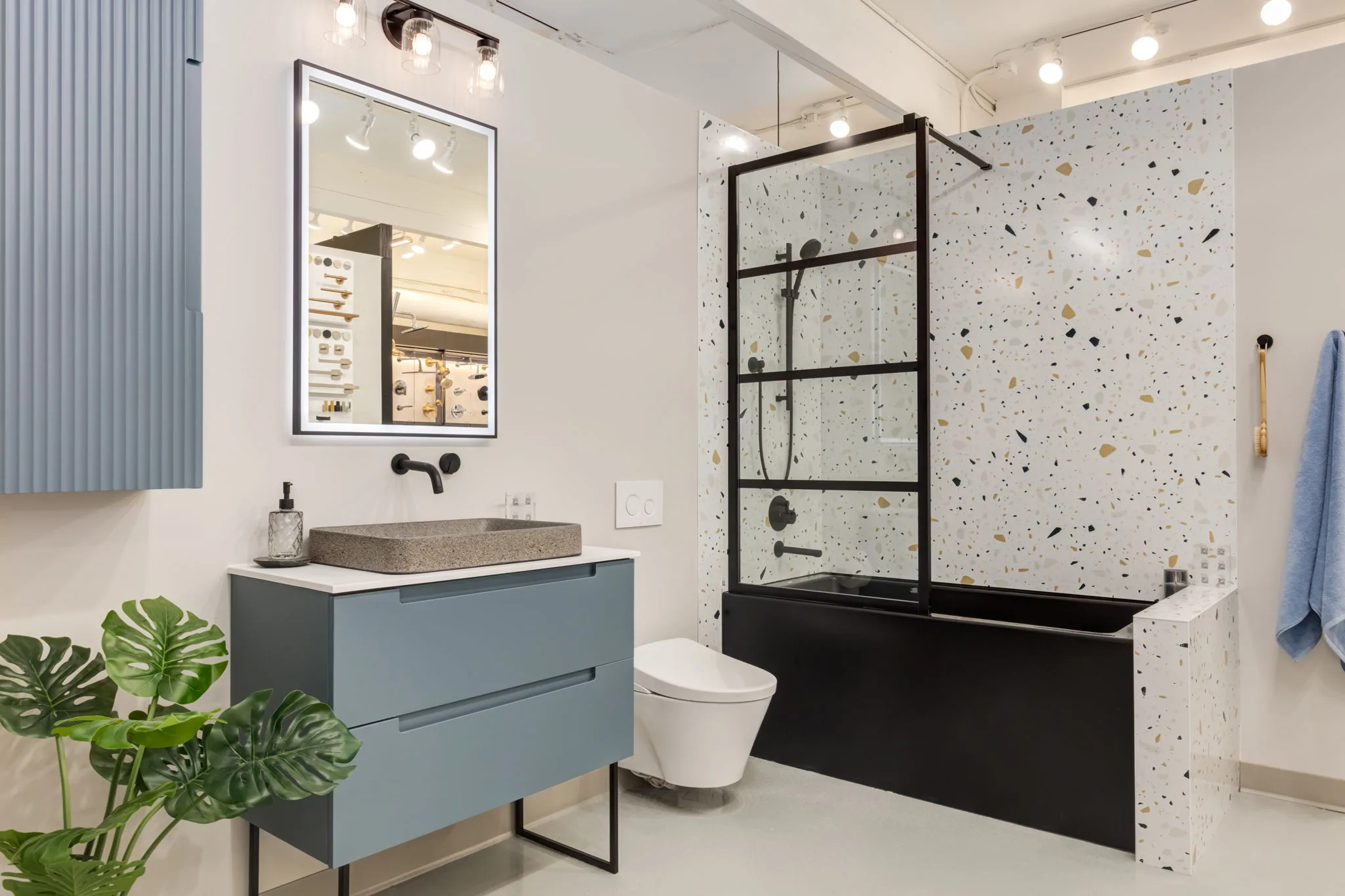 Showroom bathroom with a blue vanity, terrazzo shower wall and vessel sink
