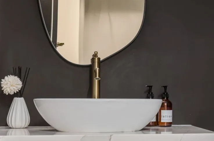 White vessel sink with a wall-mounted brass faucet and round mirror
