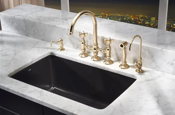 Black undermount kitchen sink with a polished brass bridge faucet on a marble countertop