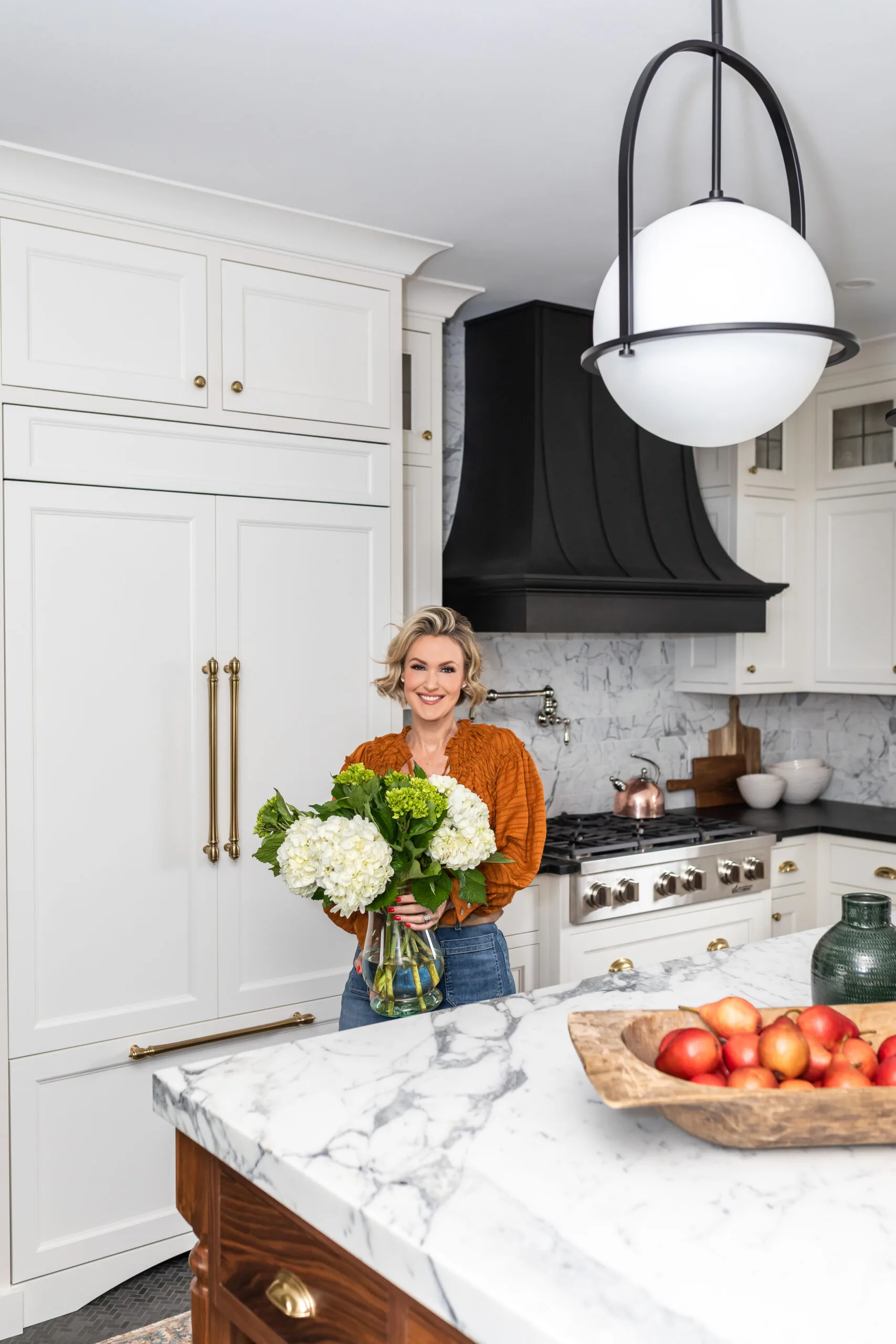 Designer Carolyn Wilbrink holding flowers in her marble-island kitchen