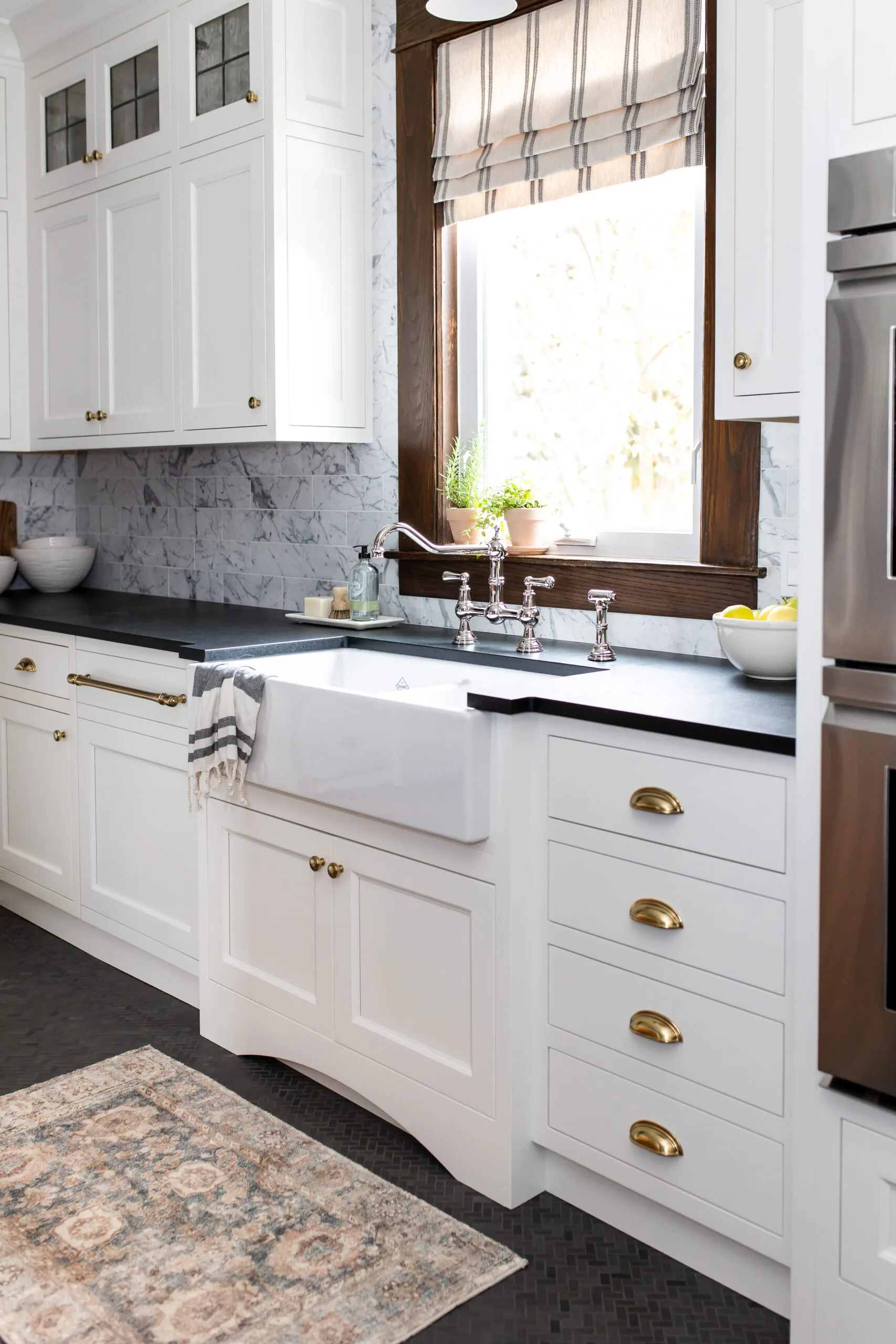 White farmhouse kitchen with an apron-front sink, marble backsplash and brass bridge faucet in Carolyn Wilbrink's project